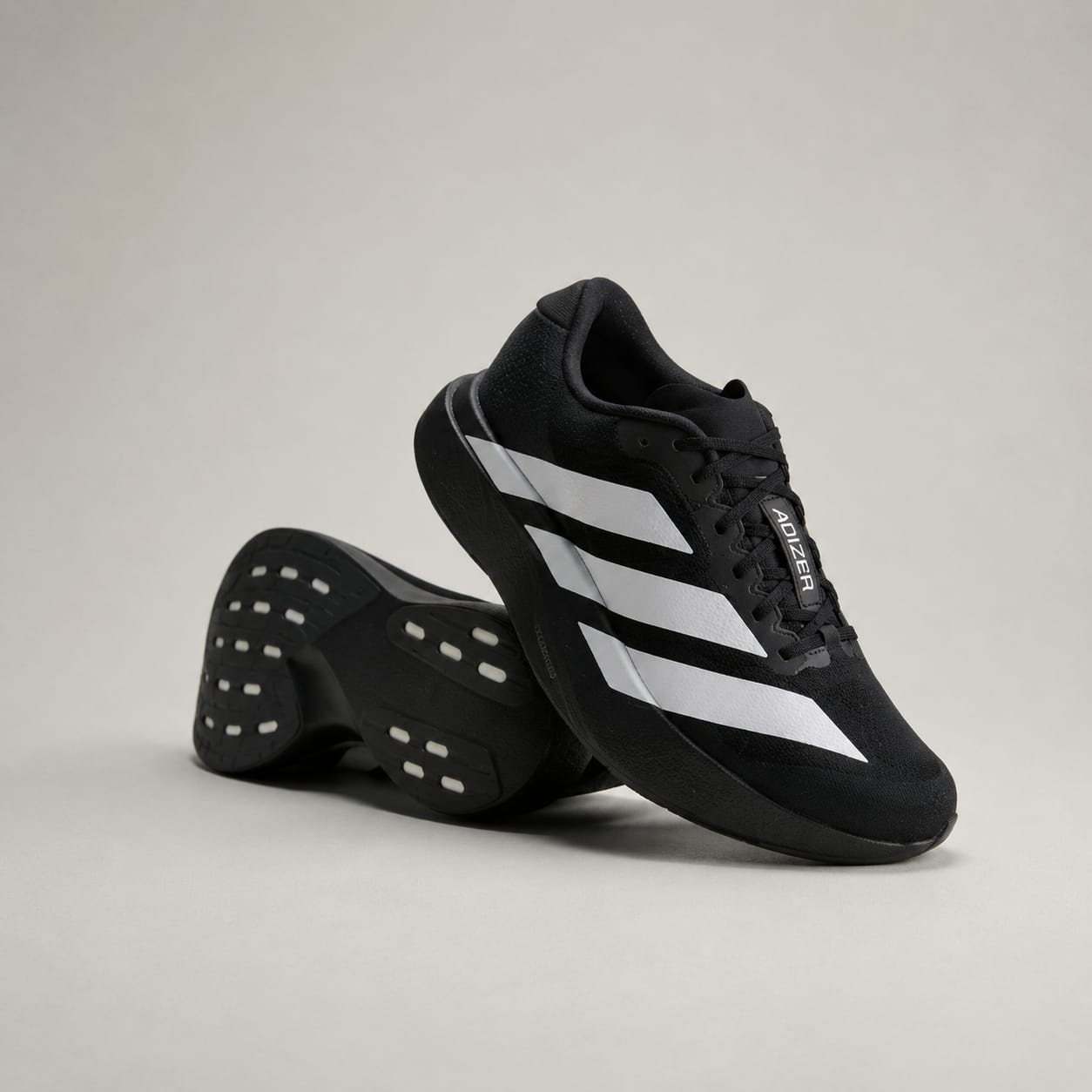 A pair of black Adidas running shoes with signature white three-stripes, shown on a neutral light gray studio background.
