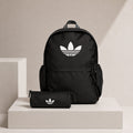 A black Adidas backpack with a white trefoil logo, displayed on a white pedestal next to a matching black pencil case with the same logo, against a beige background.