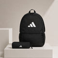 A black Adidas backpack with a white logo is displayed on a light beige pedestal alongside a matching black zippered pouch, set against a minimalist beige background.