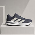 A single Adidas running shoe in navy blue and white, displayed in profile on a light gray pedestal against a neutral gray background.