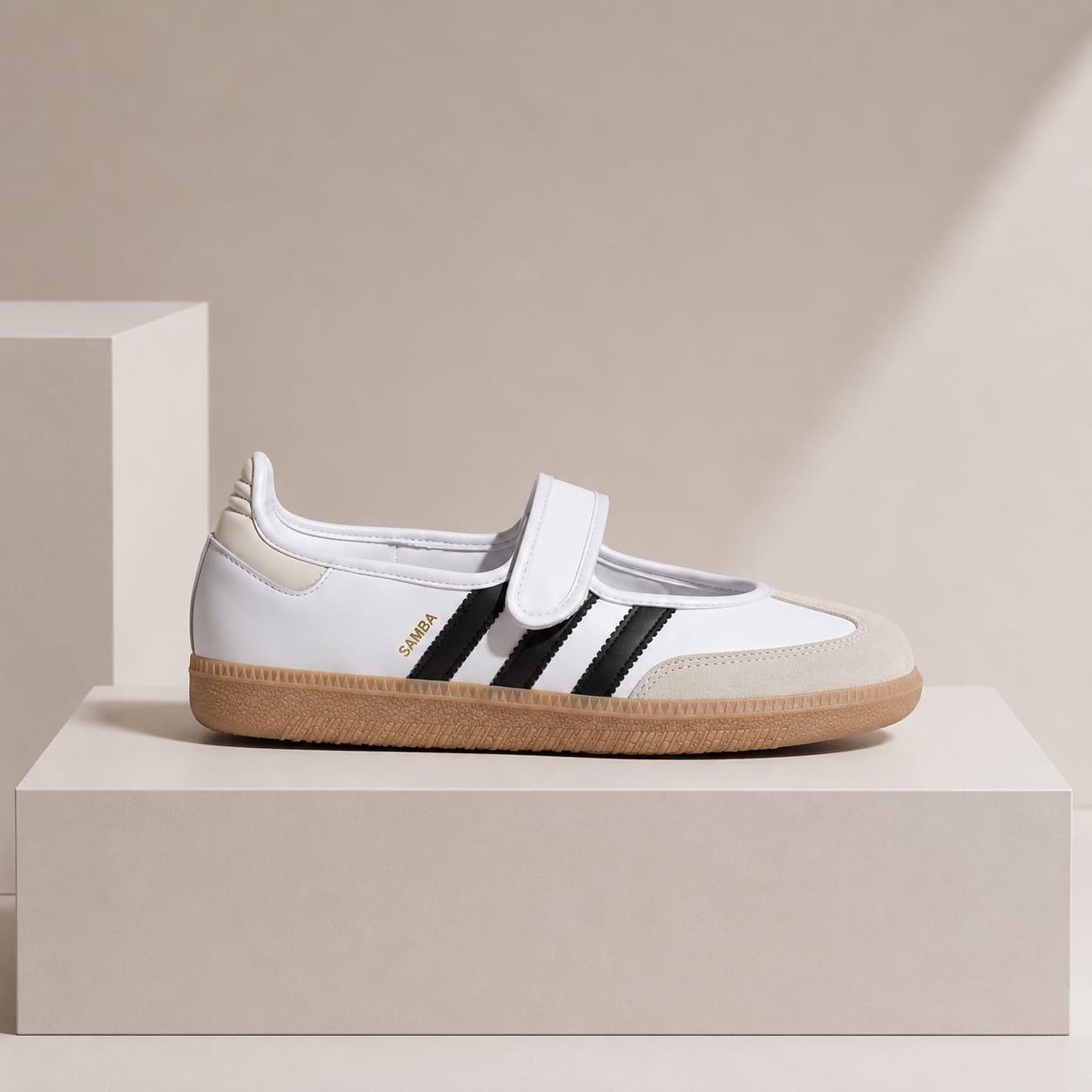 A white Adidas Gazelle sneaker with black three-stripes, a beige heel tab, and a gum sole, displayed on a minimalist beige pedestal.